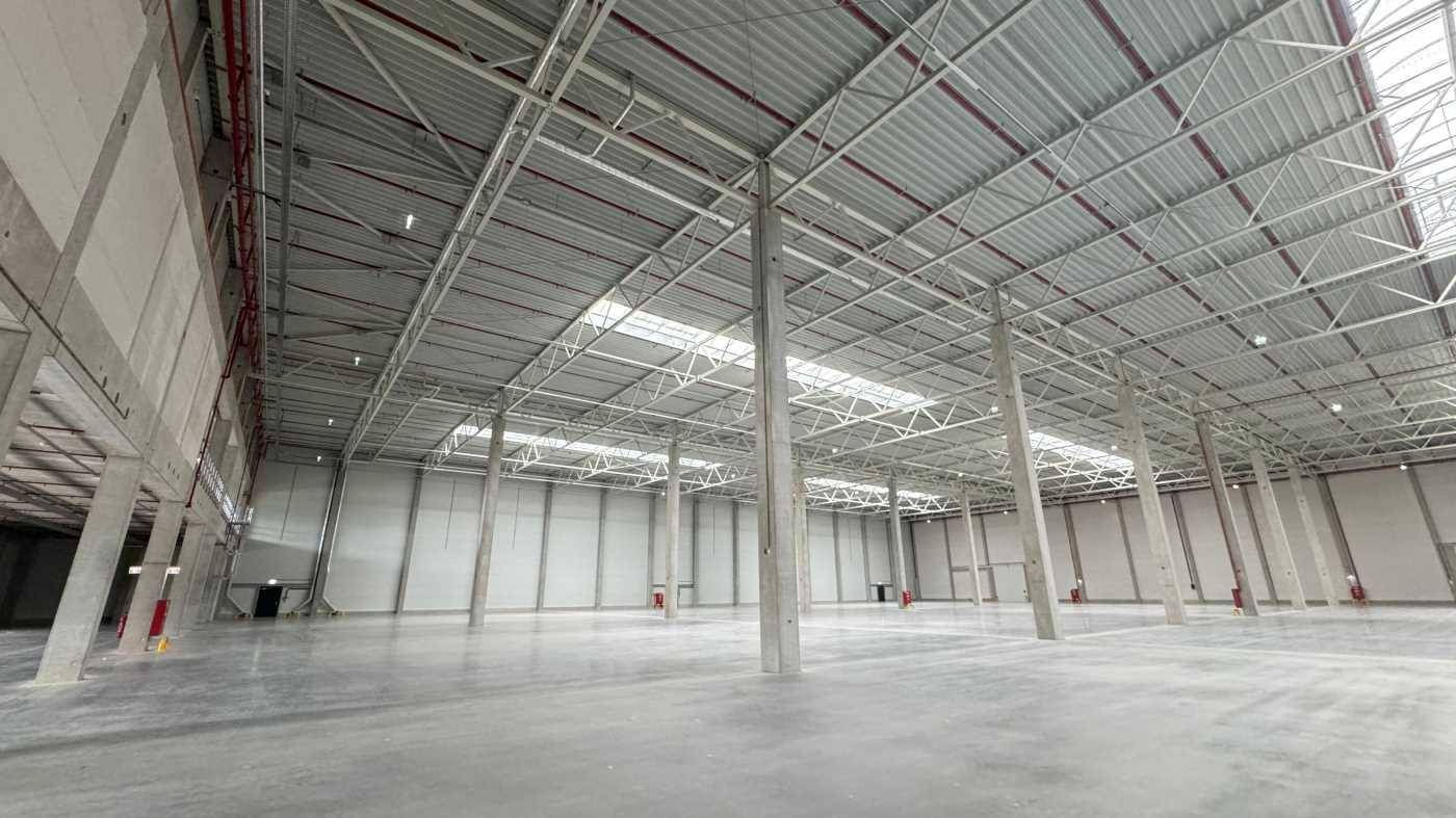 Geräumige Lagerhalle mit hohen Decken, Betonstützen und Oberlichtern, die den Raum erhellen.