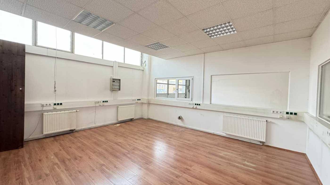 Helles Büro mit Laminatboden, Heizkörpern und hohen Fenstern für viel Tageslicht.