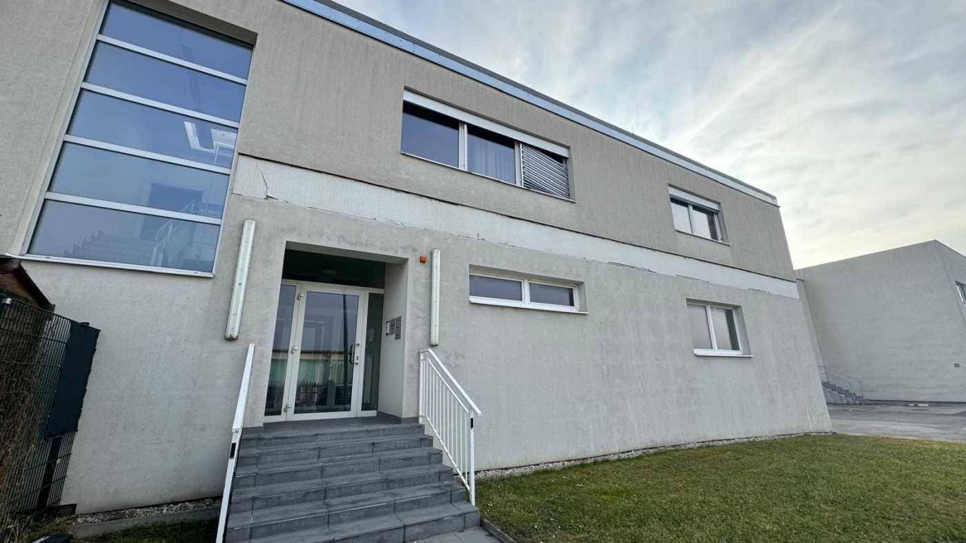 Modernes Geschäftsgebäude mit grauem Putz, großen Fenstern und einem einladenden Eingangsbereich.