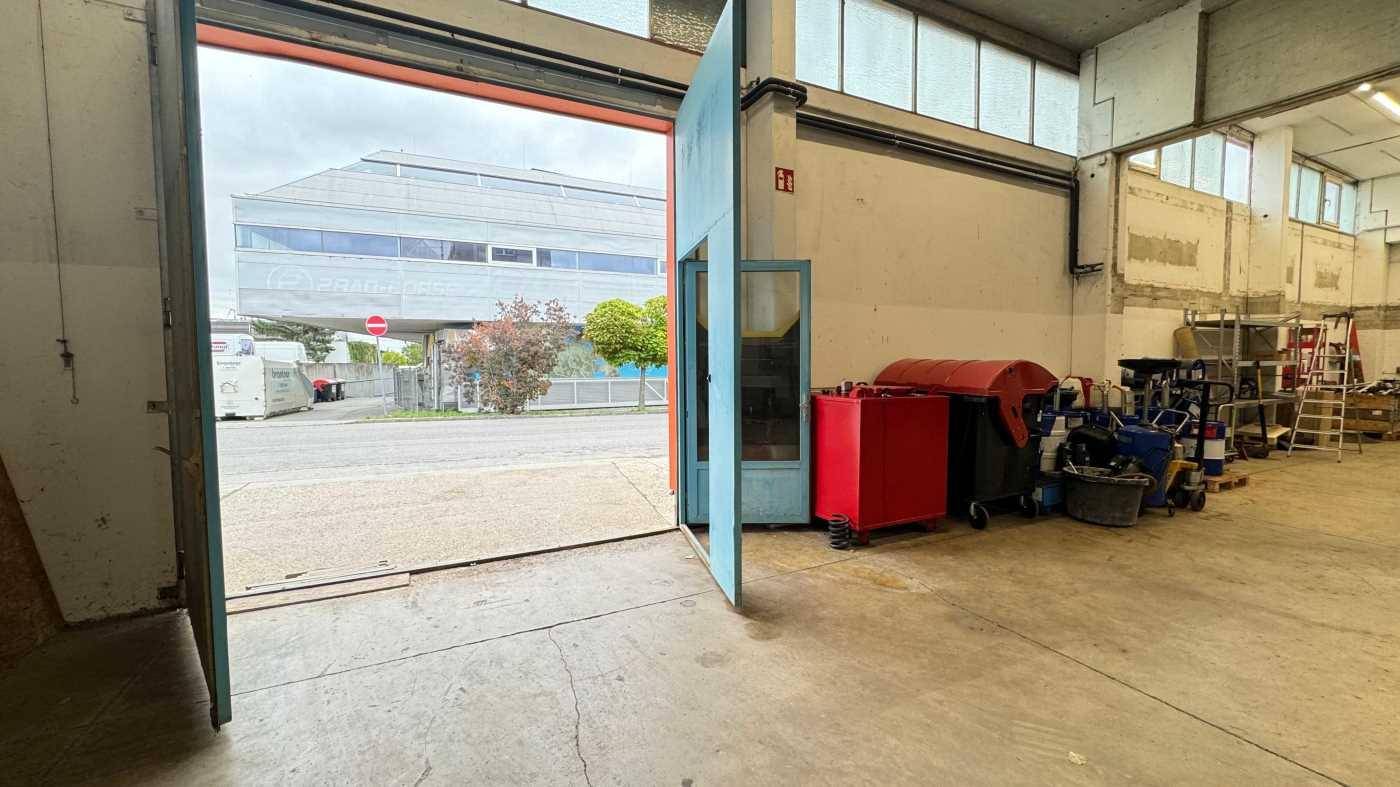 Blick aus einer Lagerhalle durch ein großes Tor auf die Straße und gegenüberliegende Gebäude.
