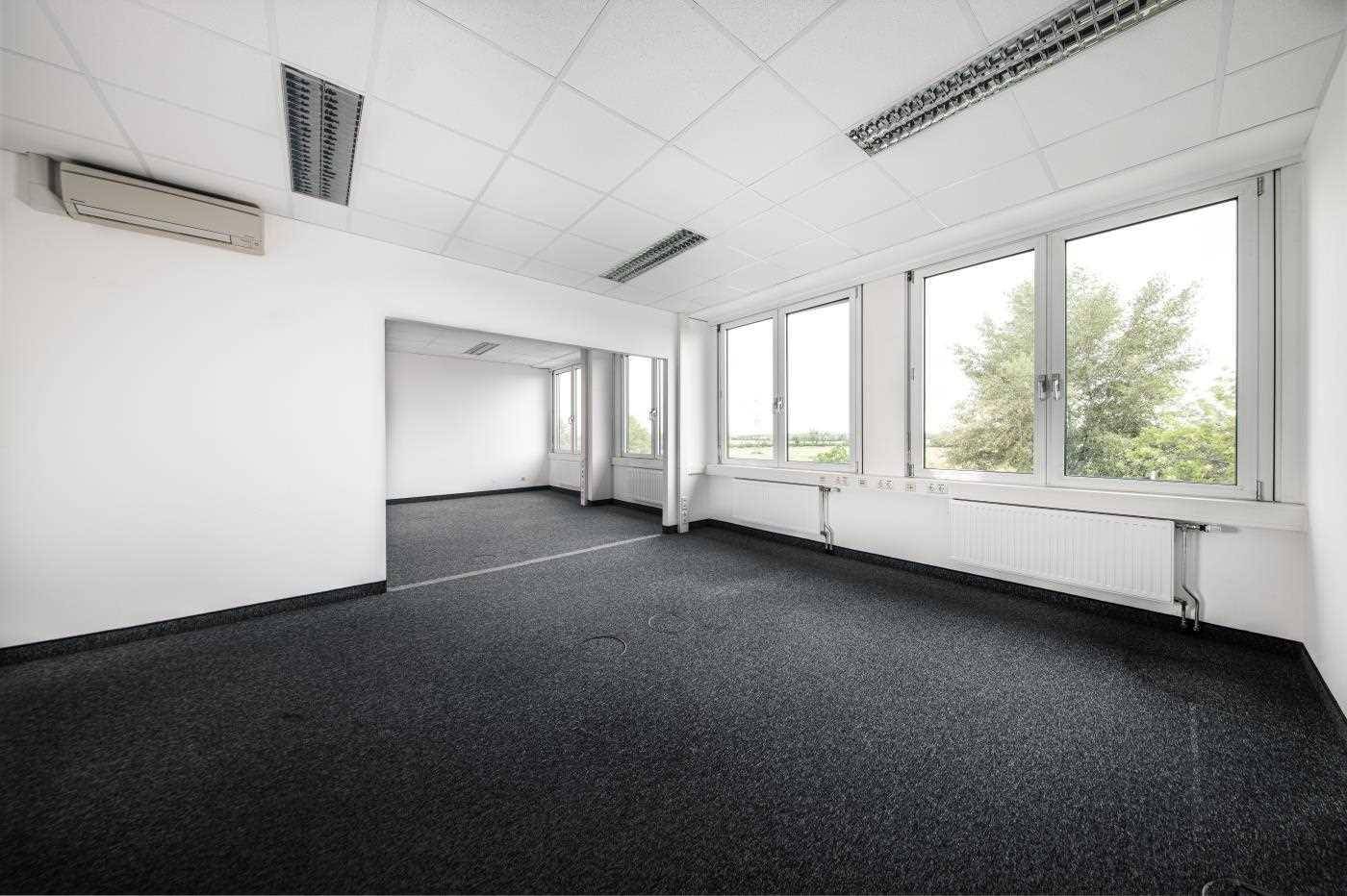 Helles, leeres Büro mit dunklem Teppichboden, großen Fenstern und Klimaanlage, bereit zur Nutzung.