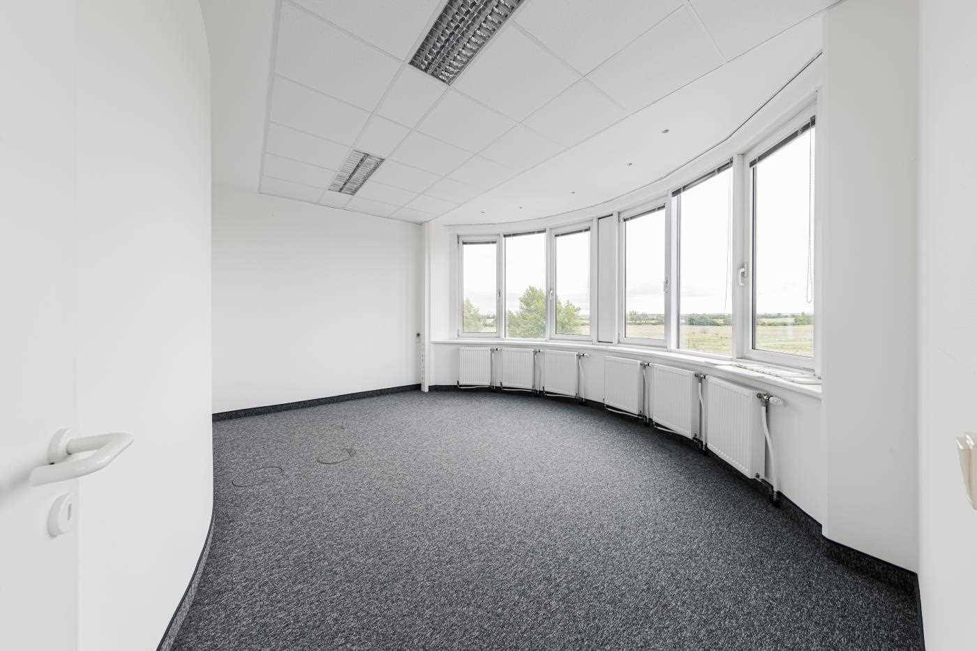 Heller Büroraum mit gebogener Fensterfront, Teppichboden und weitem Ausblick ins Grüne, ideal für eine inspirierende Arbeitsumgebung.
