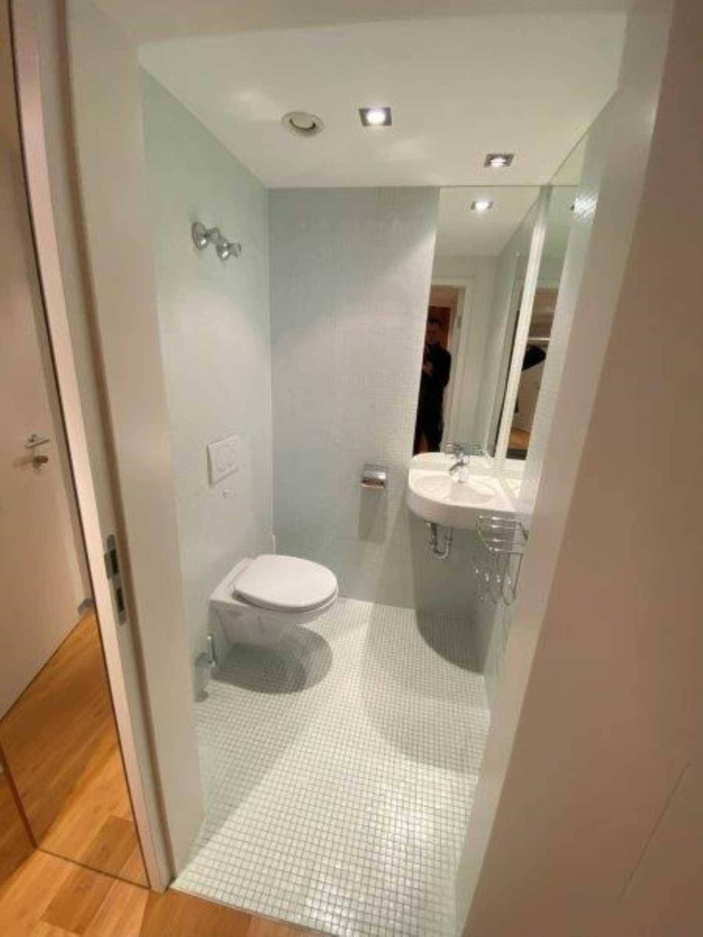 Modernes Gäste-WC mit kleinen Mosaikfliesen, wandhängender Toilette und großem Spiegel.