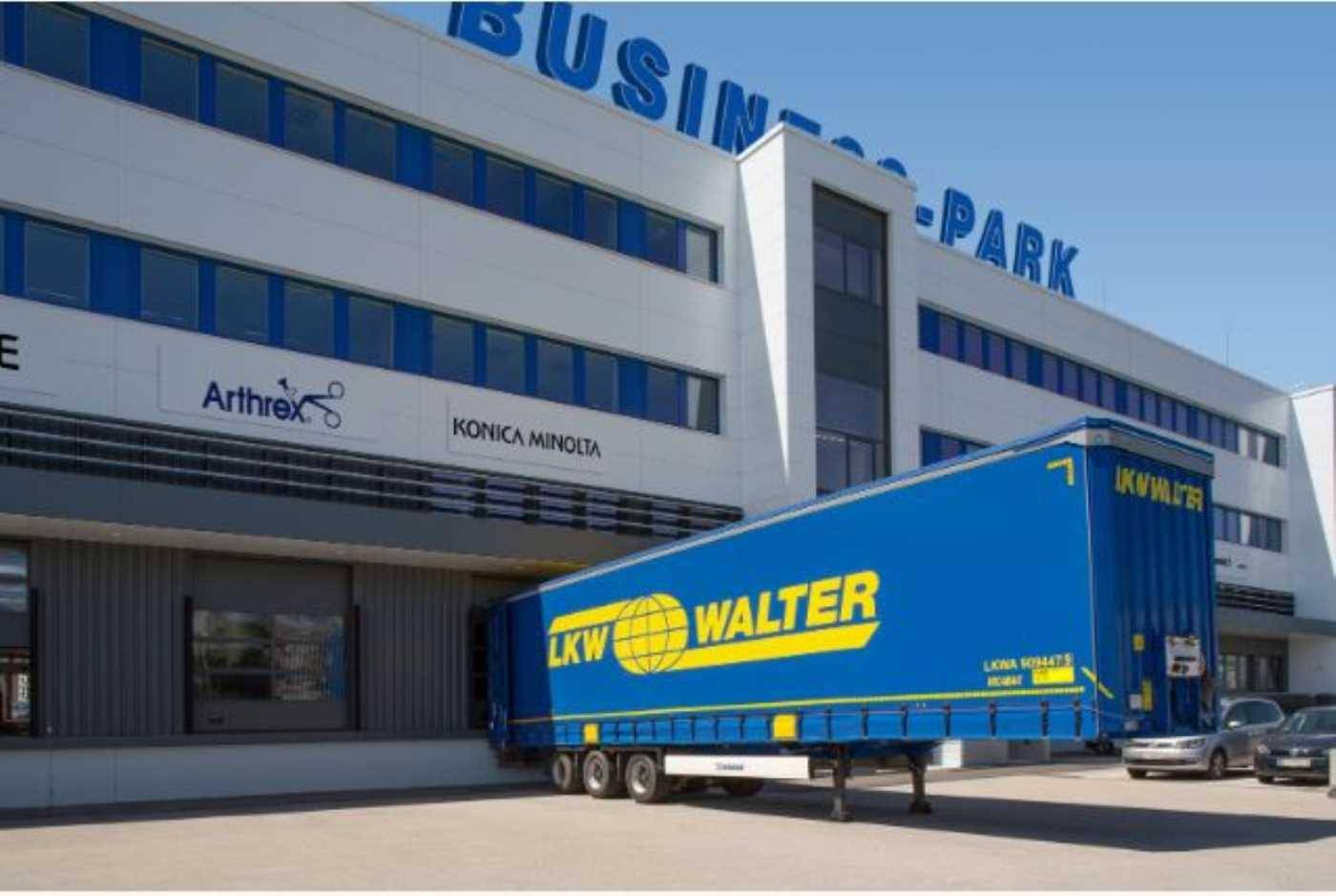 Eingangsbereich eines modernen Business-Parks mit LKW-Laderampe und Firmenlogos an der Fassade.
