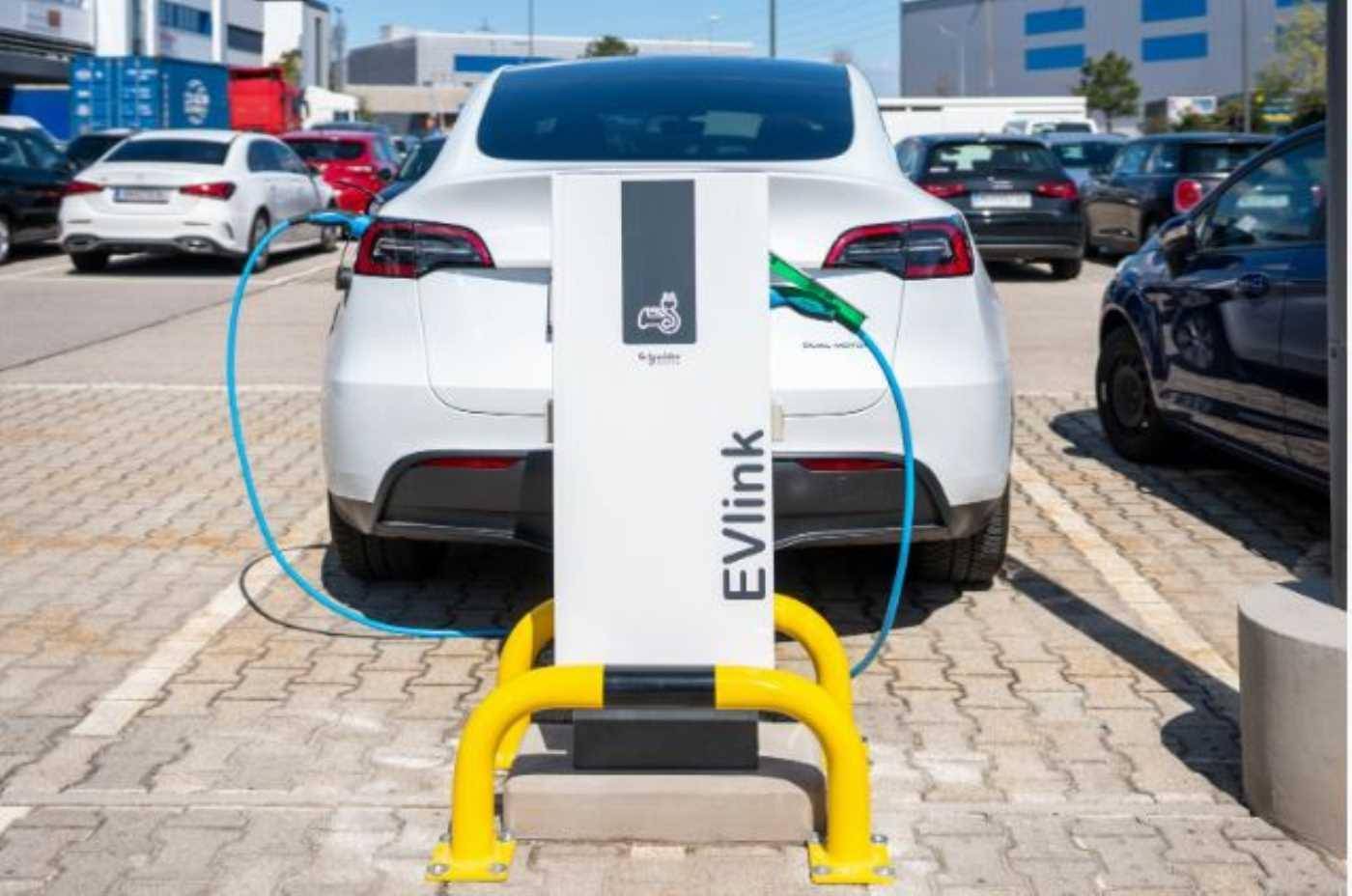 Eine Elektroauto-Ladestation auf einem Parkplatz, an der ein weißes Fahrzeug geladen wird.