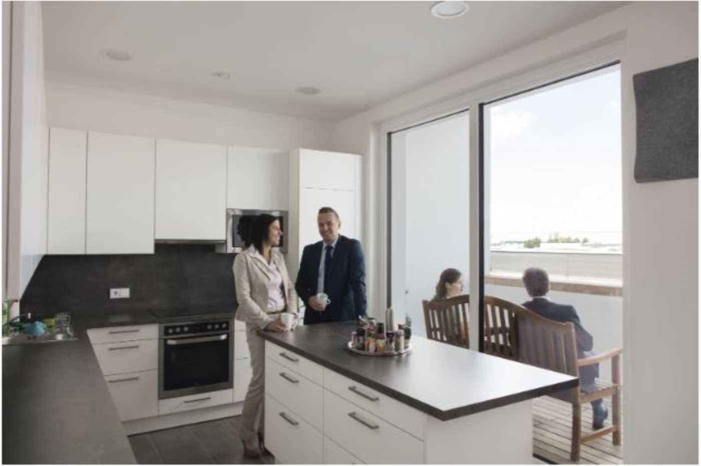 Moderne Einbauküche mit weiß-grauen Fronten, Kücheninsel und Zugang zu einem Balkon mit Sitzgelegenheiten.