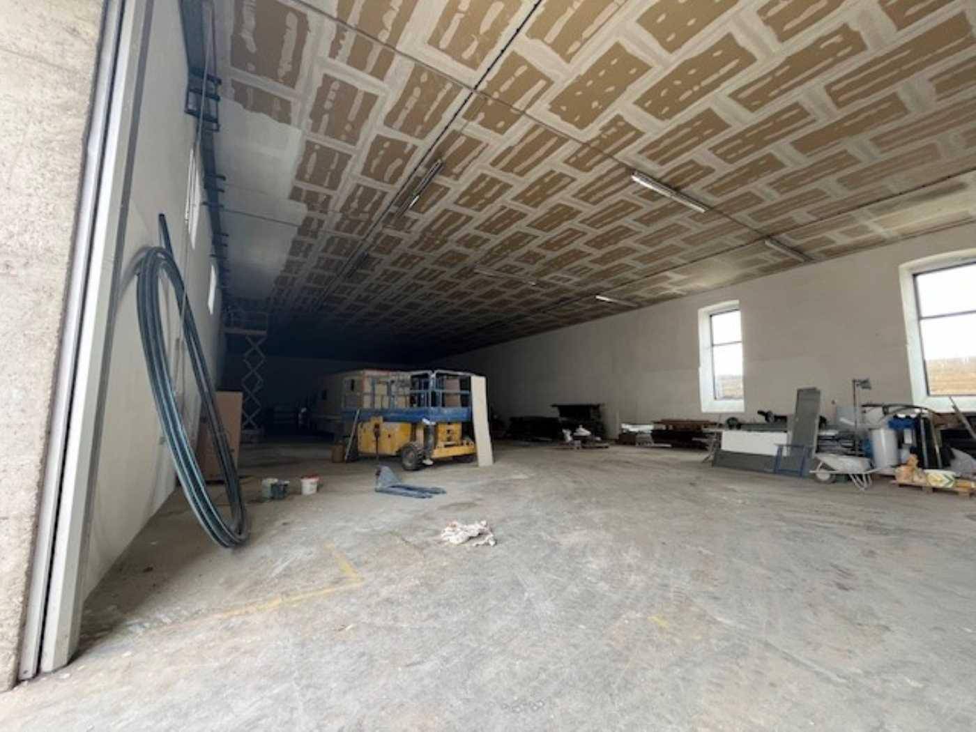 Geräumiger Lagerraum mit Betonboden und hohen Decken, teilweise mit Baumaterialien gefüllt und Tageslicht.