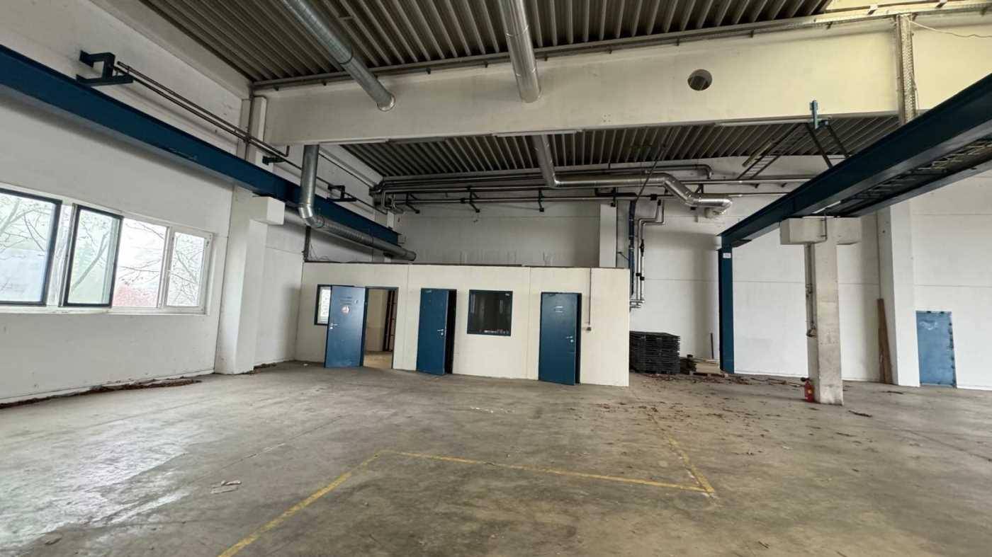 Industrielle Halle mit hohen Decken, sichtbaren Leitungen und abgetrennten Büroräumen.