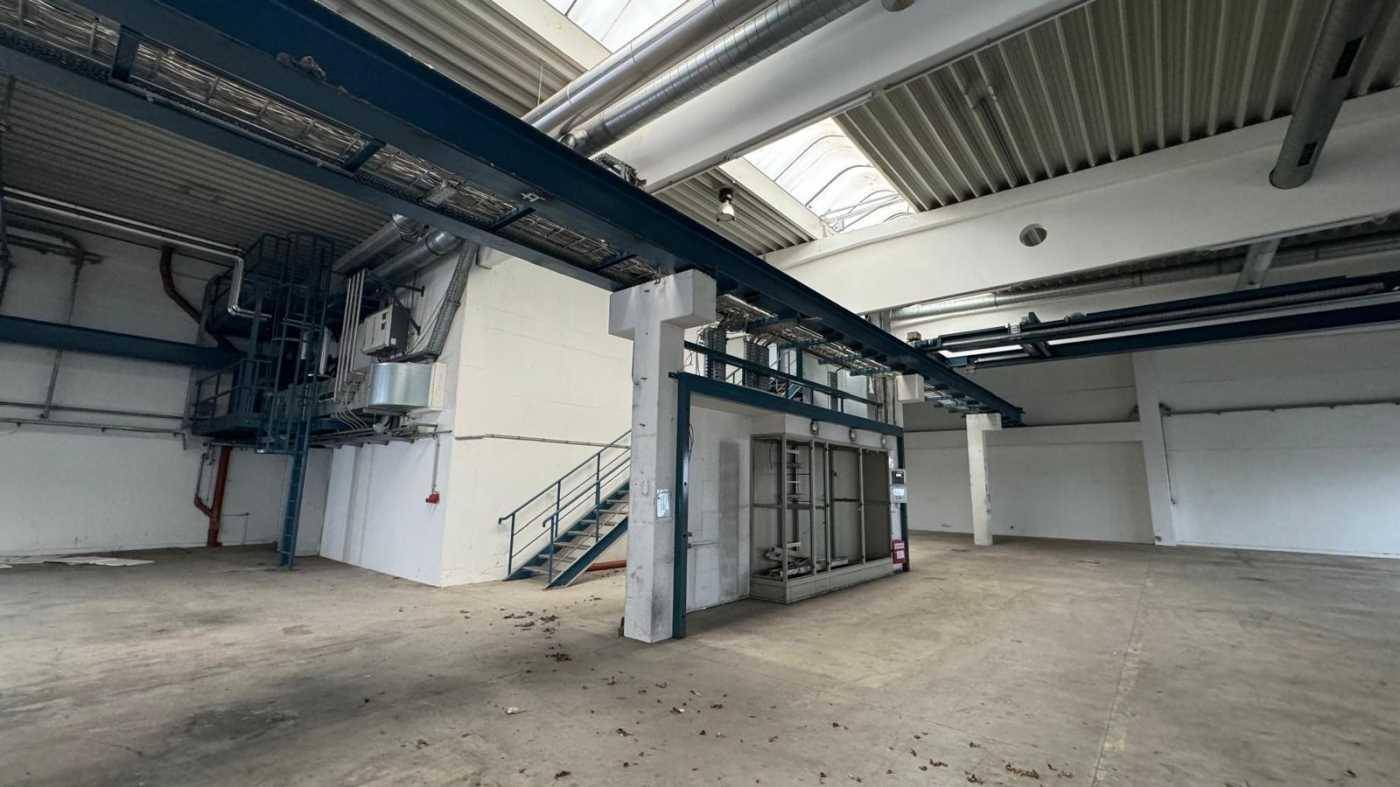 Geräumige Industriehalle mit hohen Decken, Kranbahn und Treppenaufgang zu einer Zwischenebene.