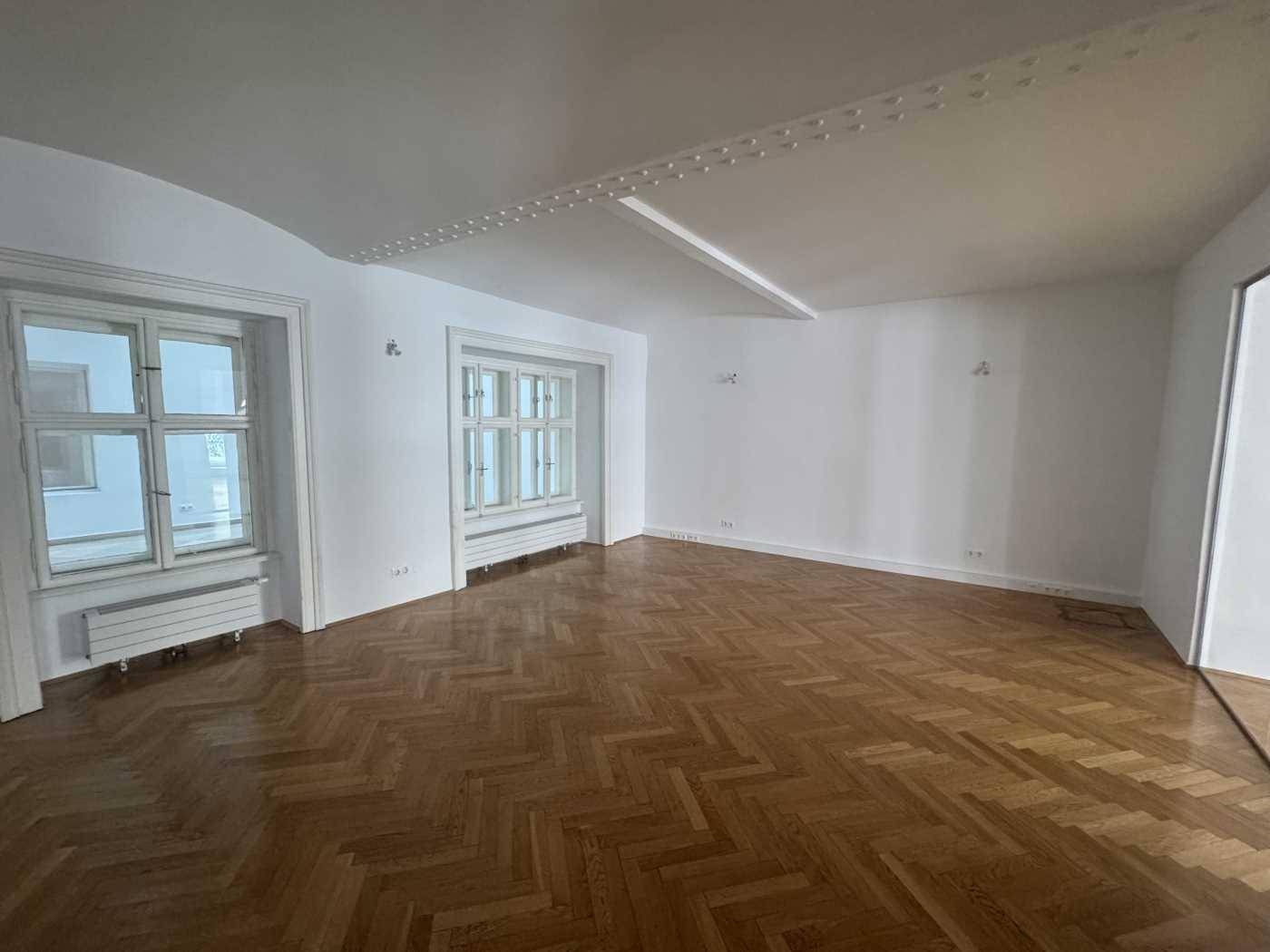 Großer, leerer Raum mit glänzendem Fischgrätparkett und dekorativer Deckenleiste, die Eleganz verleiht.