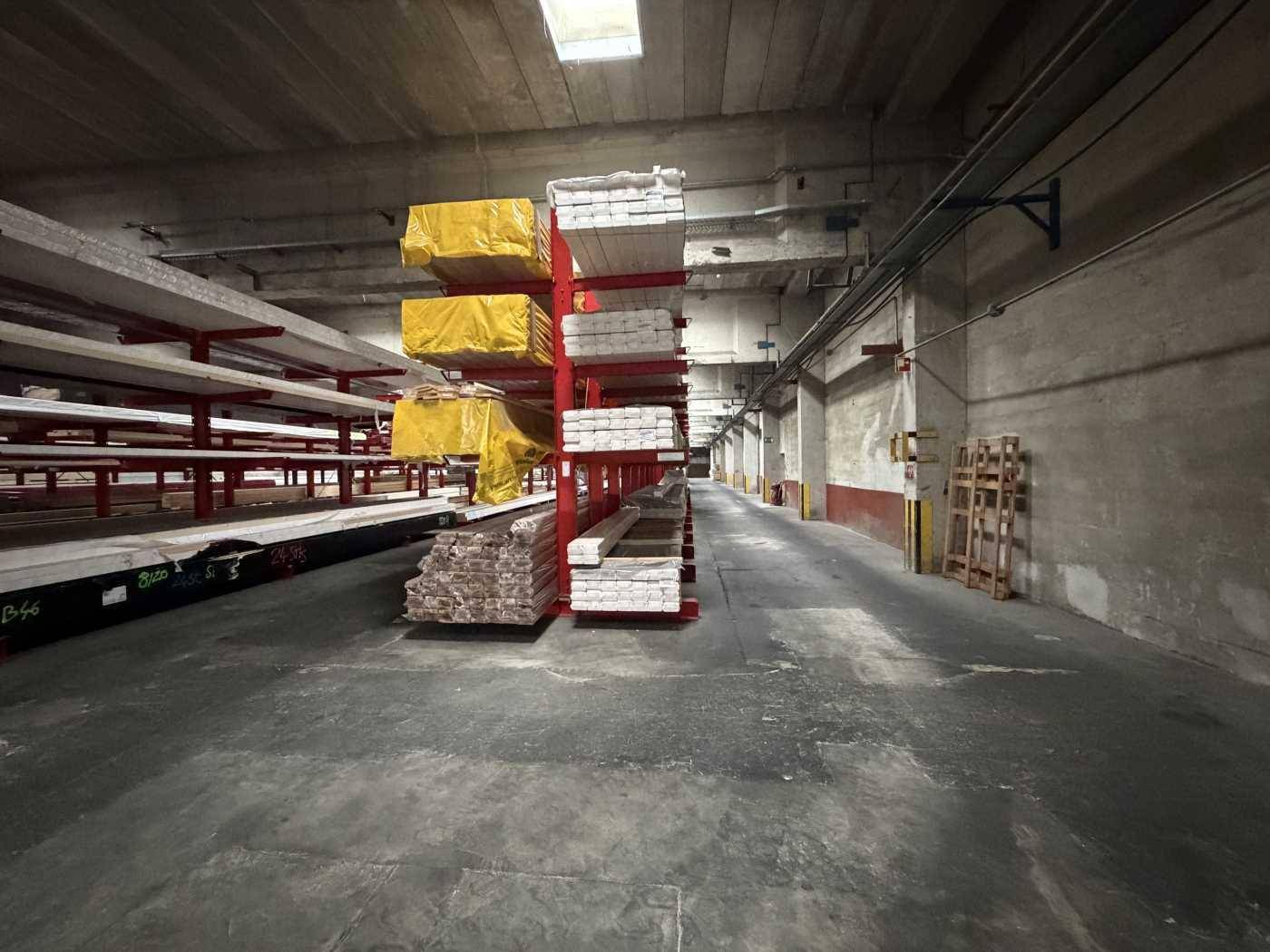 Blick in eine Lagerhalle mit Betonwänden, hohen Regalen und ordentlich gestapelten Baumaterialien.