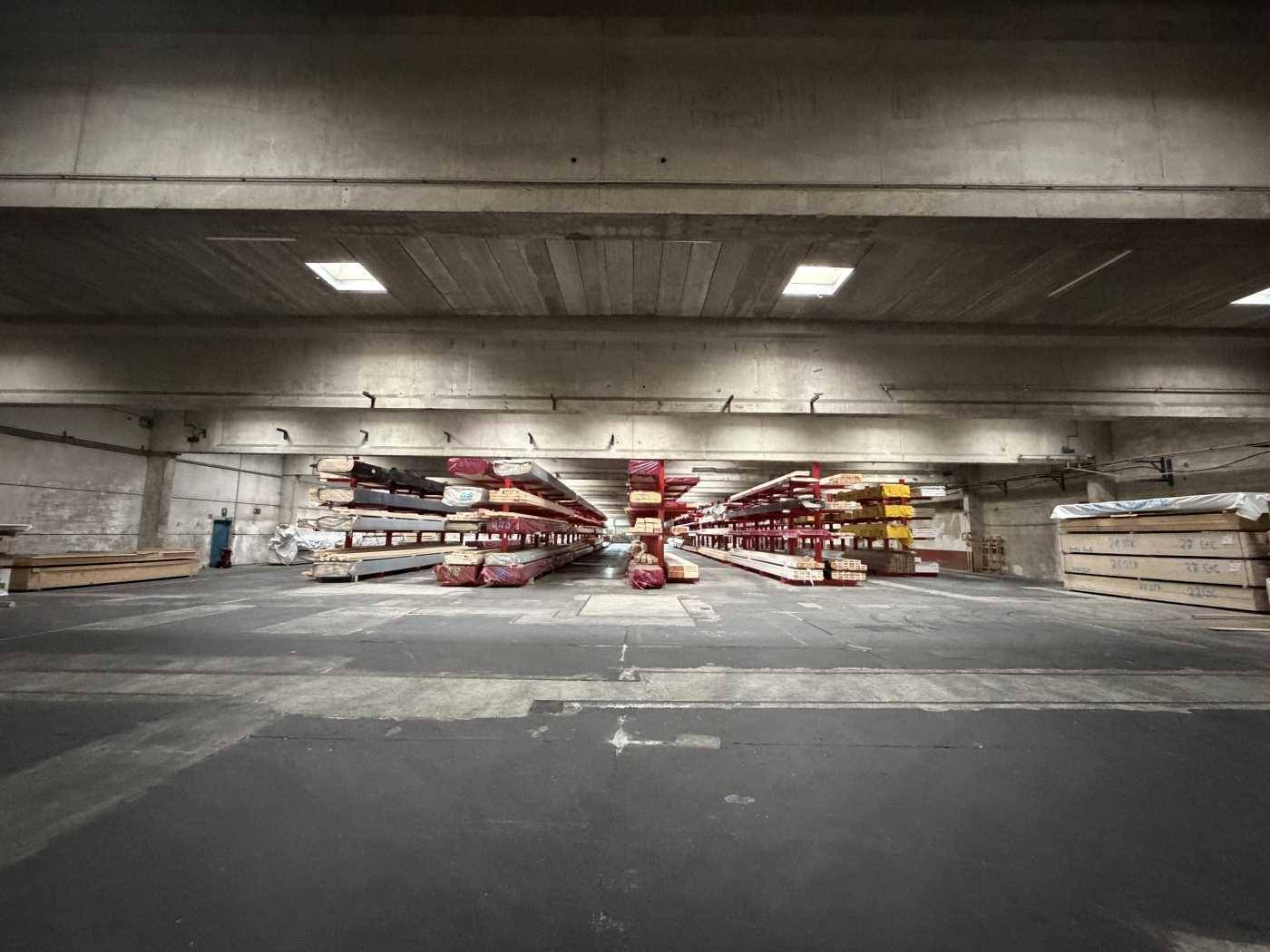 Geräumige Lagerhalle mit hohen Decken, Betonboden und gestapelten Materialien auf robusten Regalen.