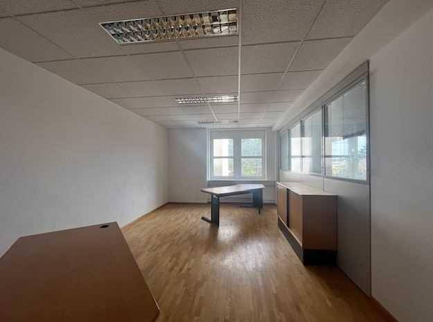Heller Büroraum mit Holzboden, großen Fenstern und abgehängter Decke, bereit zur Einrichtung.