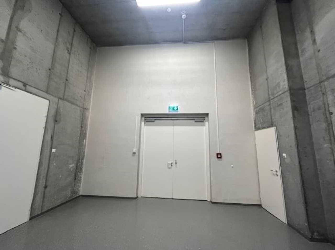 Kellerraum mit Sichtbetonwänden und einer großen Doppeltür, geeignet für Lagerung oder Technikräume.