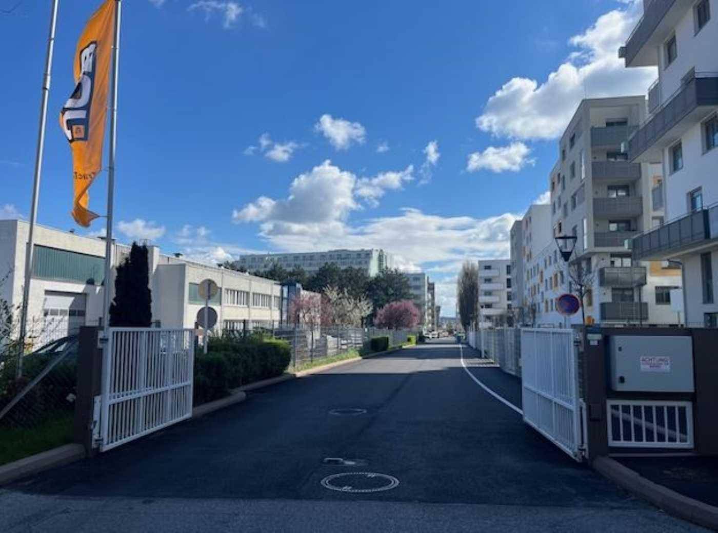 Blick auf eine Zufahrtsstraße in einem Gewerbegebiet mit verschiedenen Gebäuden und einem Fahnenmast.