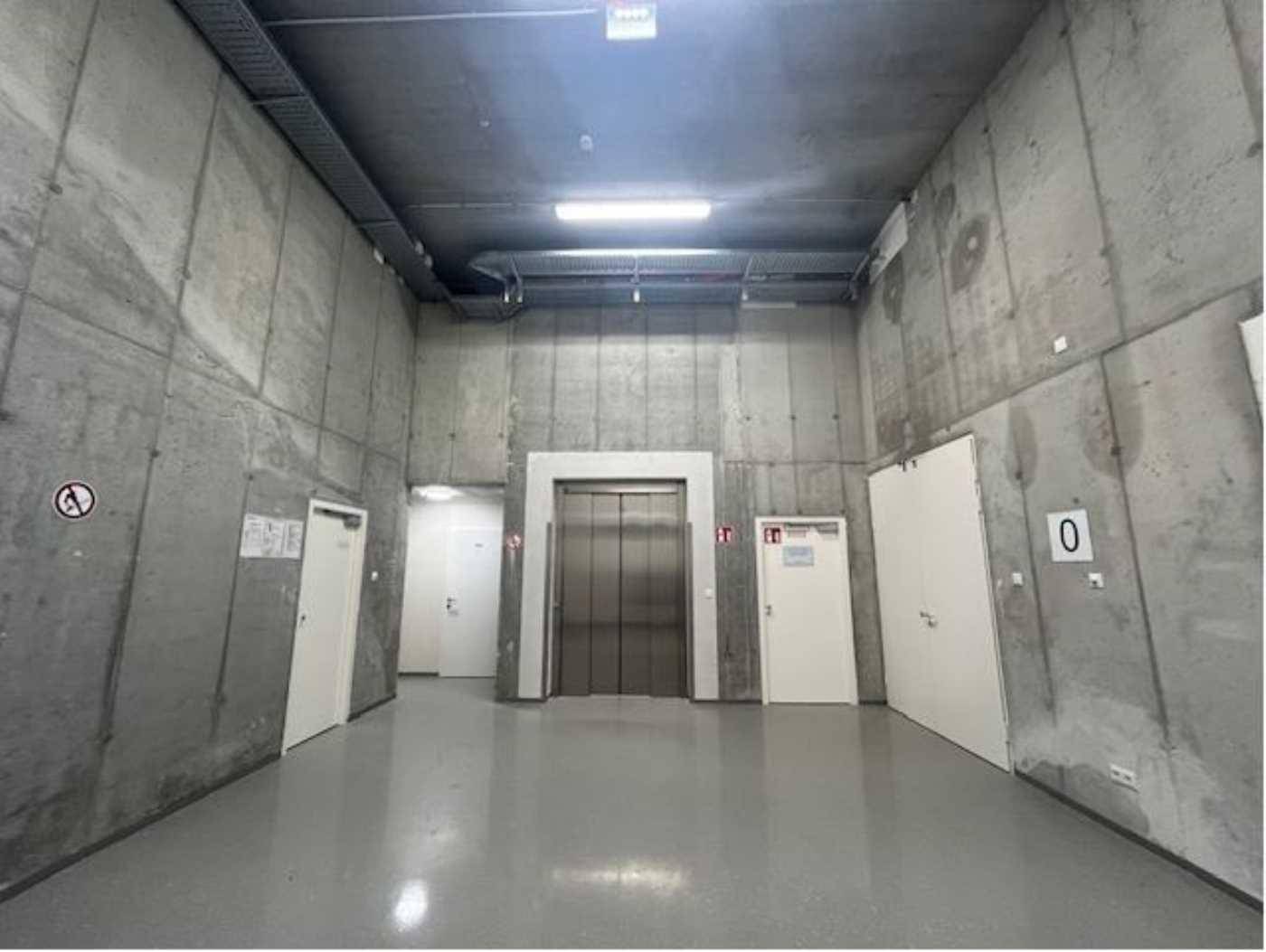 Funktionaler Kellerbereich mit Sichtbetonwänden, Aufzug und mehreren Türen, ideal für Lagerung oder Technik.