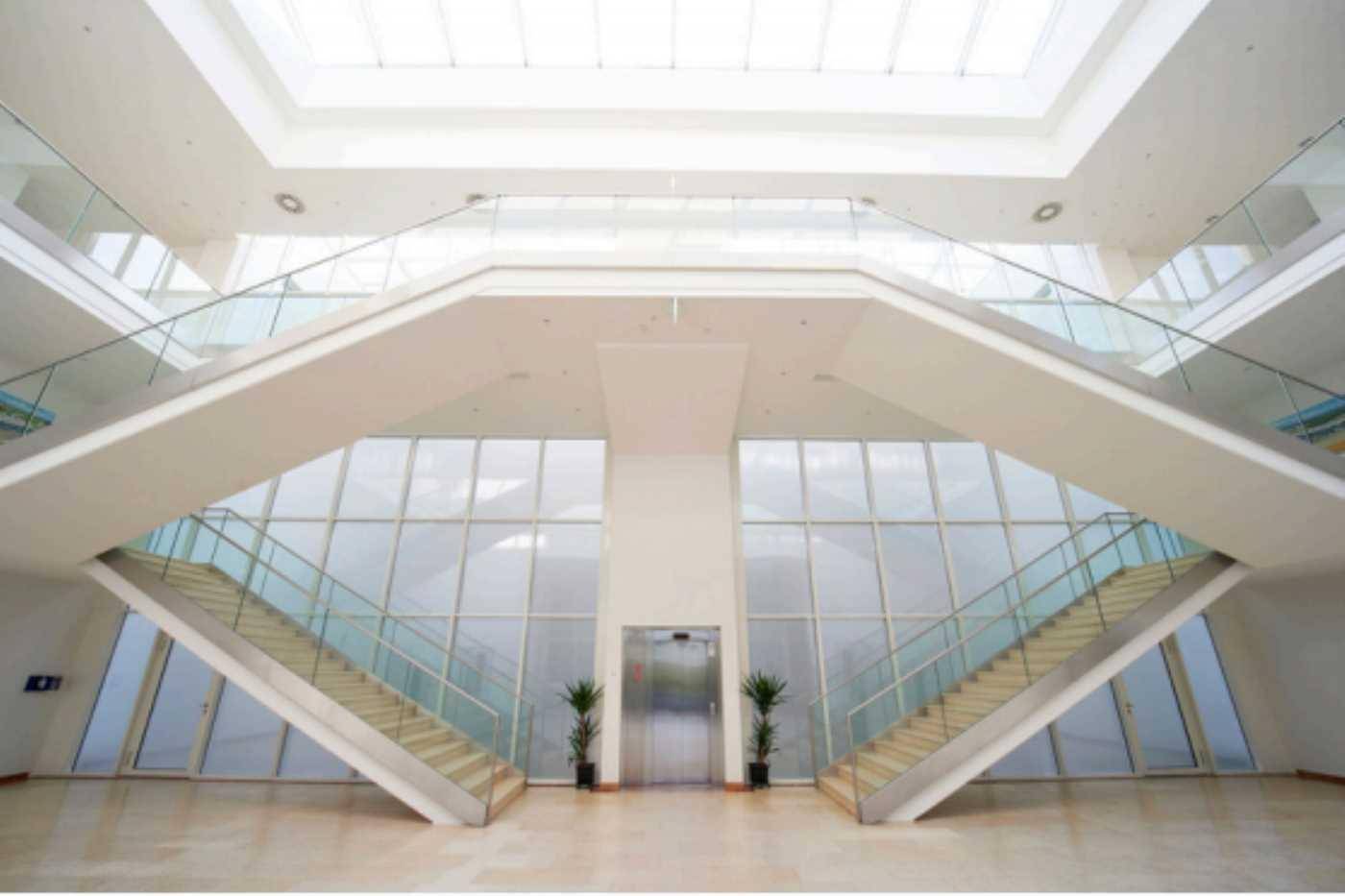 Großzügige Eingangshalle mit doppelter Treppe, Glasfassade und zentralem Aufzug.