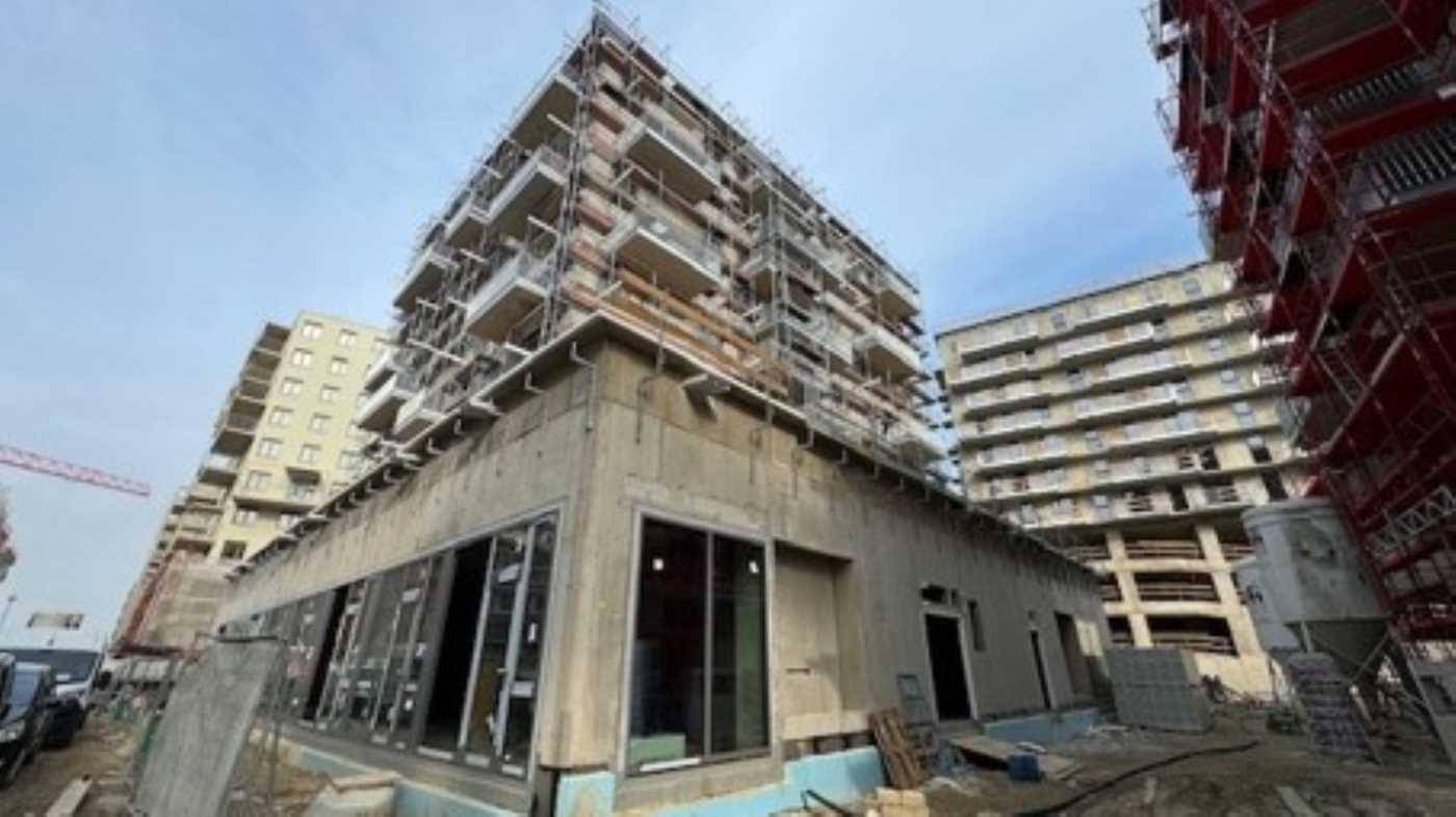 Neubau mit großen Fensterfronten im Erdgeschoss und Balkonen in den oberen Etagen, umgeben von Gerüsten.