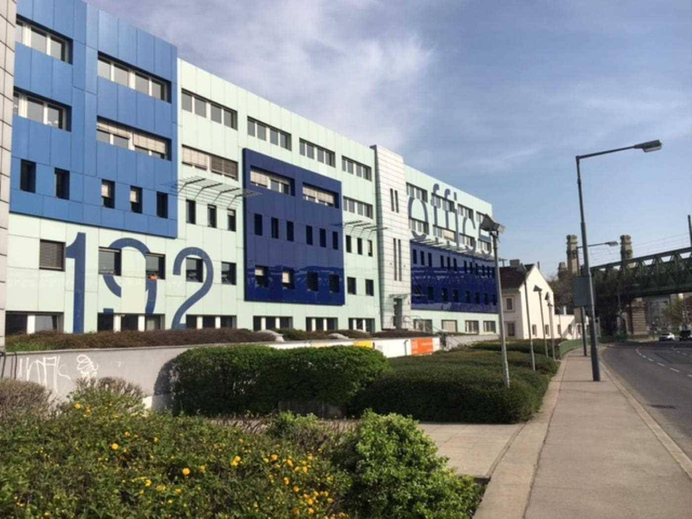 Ansicht des modernen Bürogebäudes von der Straße aus, umgeben von Grünflächen und einem Gehweg.