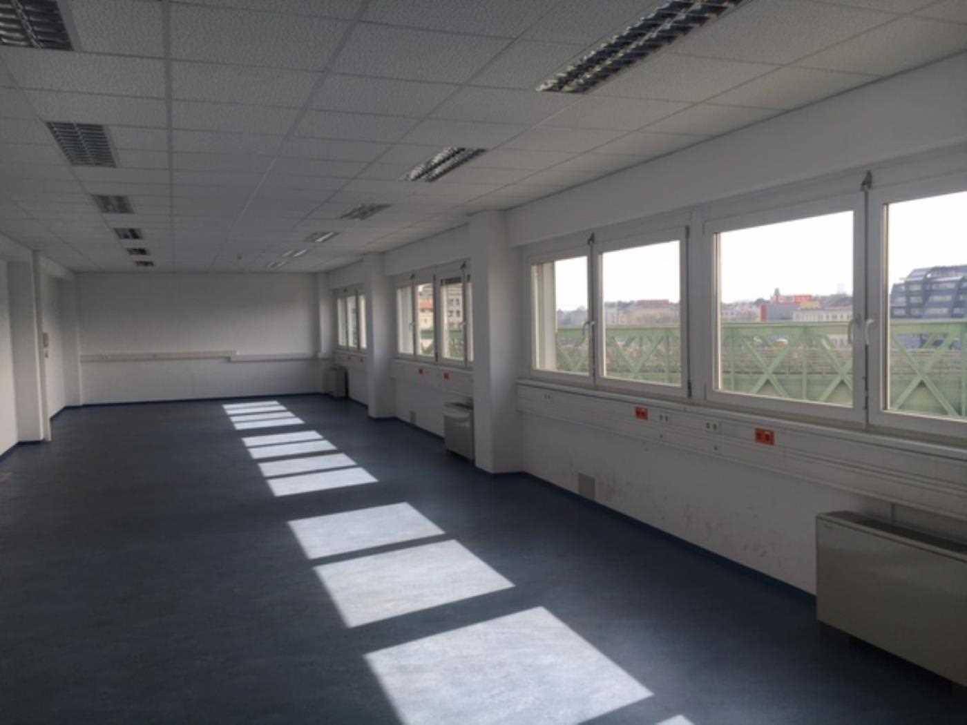 Leeres Büro mit dunkelblauem Teppichboden, weißen Wänden und Fenstern, die einen Blick nach draußen bieten.