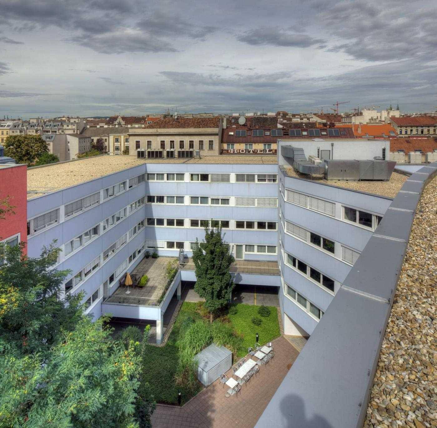 Luftaufnahme eines begrünten Innenhofs mit Sitzgelegenheiten, umgeben von Bürogebäuden und Stadtblick.
