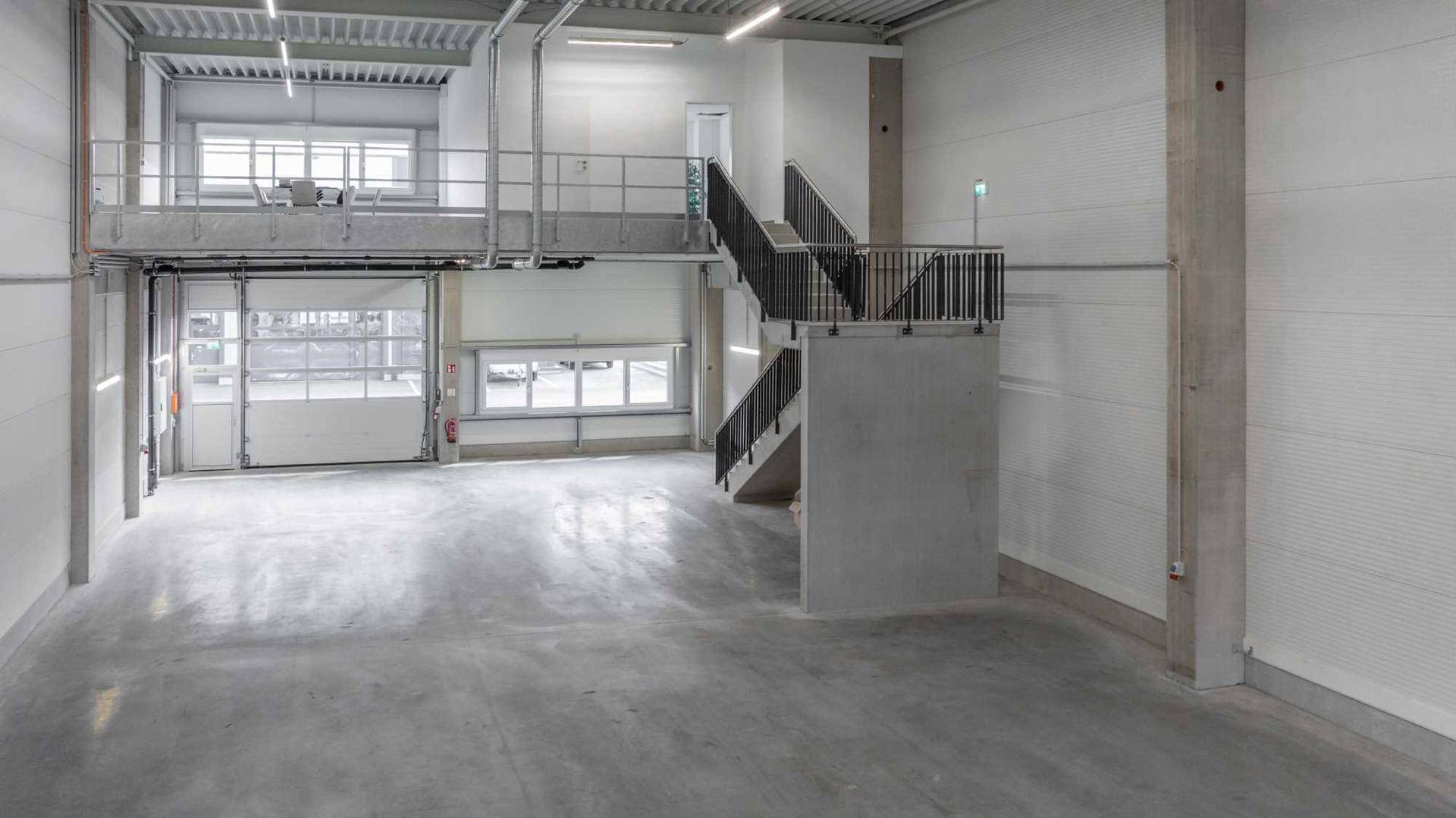 Helle und geräumige Lagerhalle mit hohen Decken, Betonboden, einer Galerie und einer robusten Treppe.