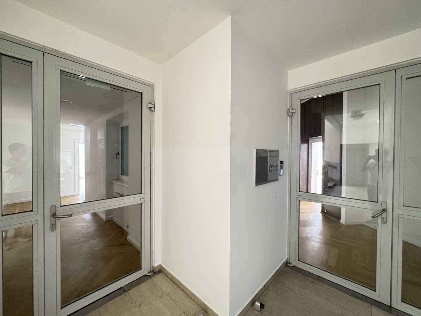 Eingangsbereich mit modernen Glastüren, hellem Boden und Gegensprechanlage für sicheren Zugang.
