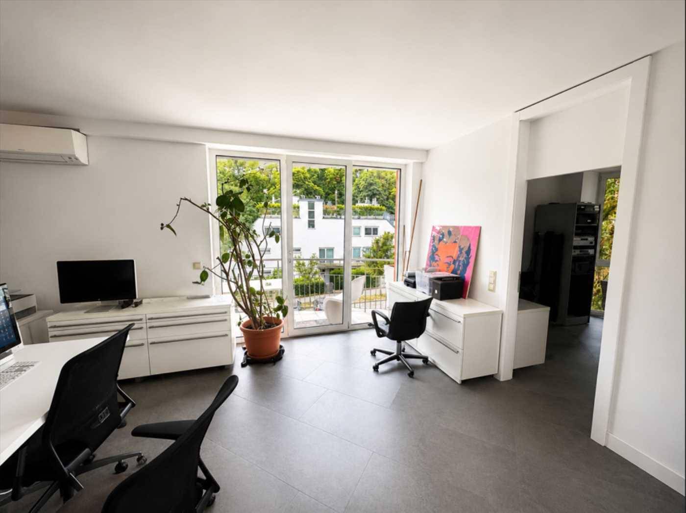 Helles Büro mit großem Fenster, Zugang zum Balkon und modernen Büromöbeln.