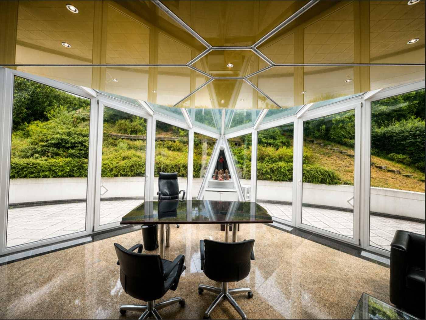 Modernes Büro mit Glaswänden und Blick ins Grüne, ausgestattet mit einem großen Schreibtisch.