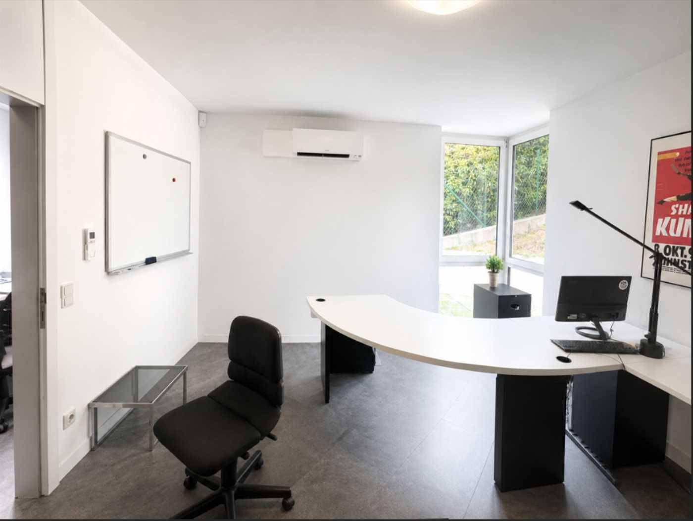 Helles und minimalistisches Büro mit weißer Tafel, Klimaanlage und Blick ins Grüne.