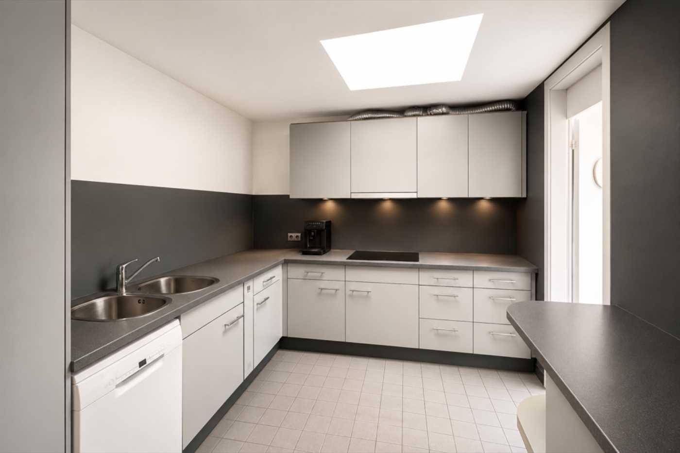 Moderne Küche mit weißen Schränken, grauen Arbeitsplatten und einem Oberlicht für natürliches Licht.