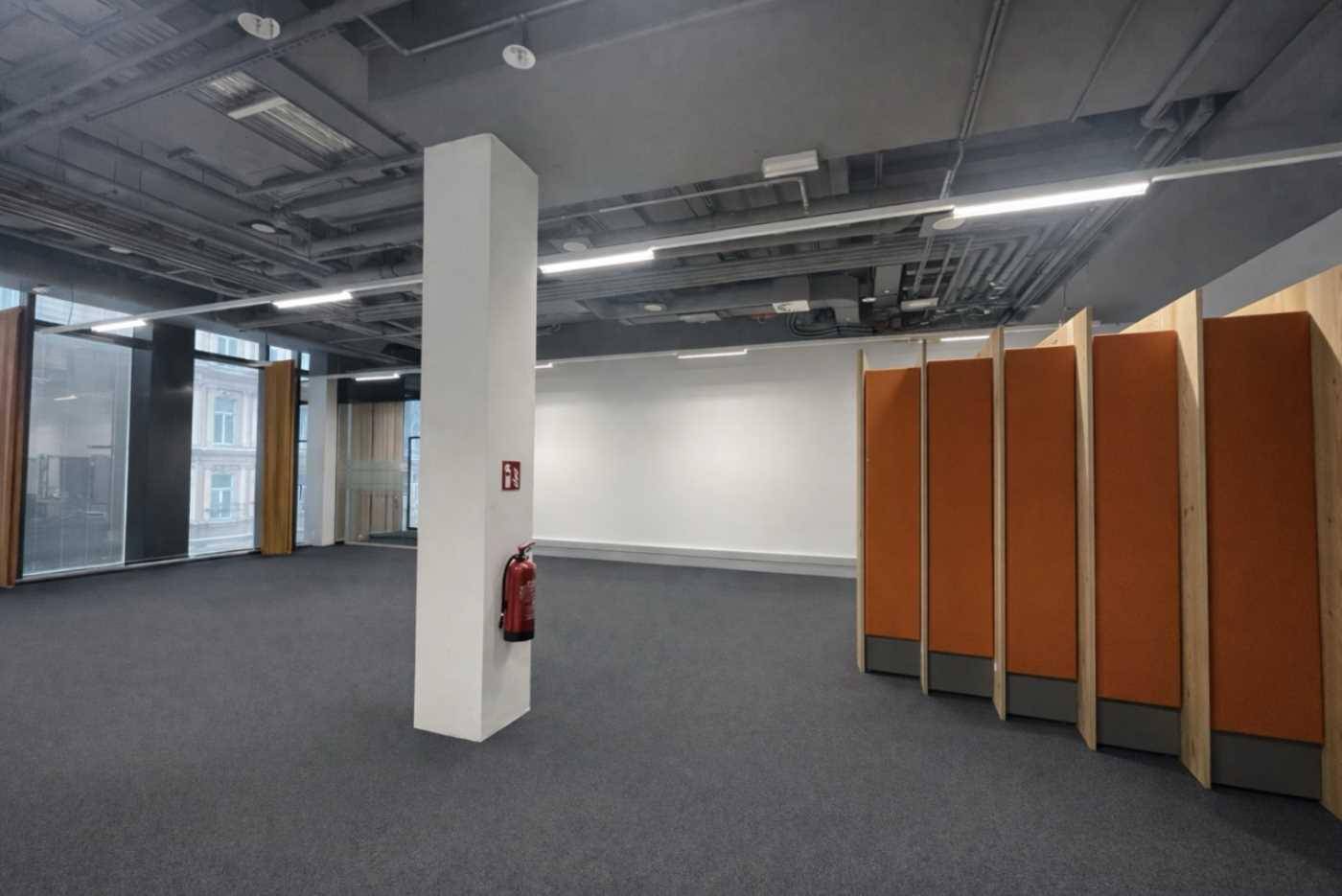 Großer, leerer Büroraum mit Teppichboden, Säule und flexiblen Raumteilern in warmen Farbtönen.