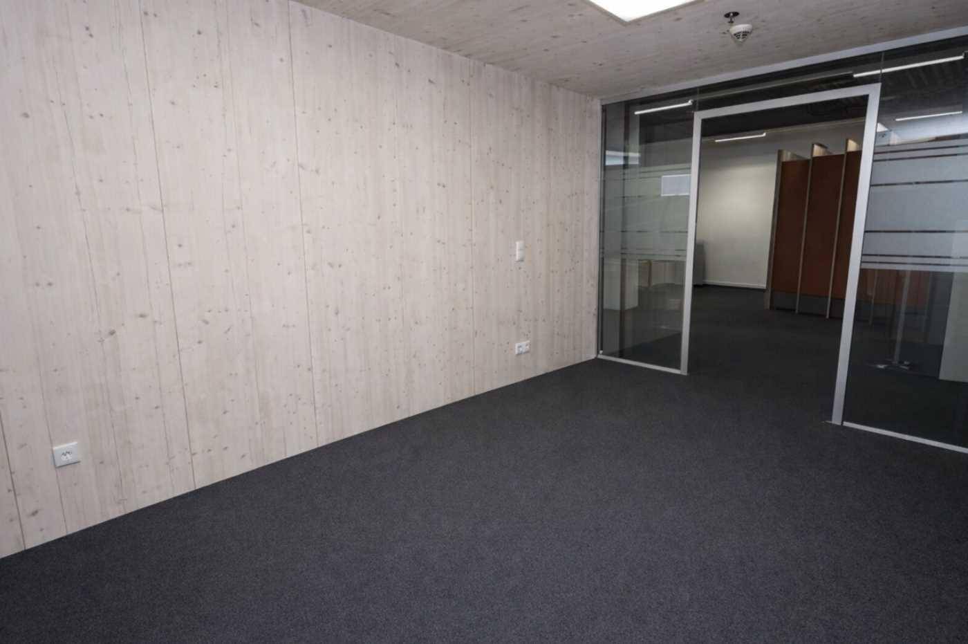 Büroraum mit Teppichboden, Holzwänden und Glastüren, die zu weiteren Arbeitsbereichen führen.