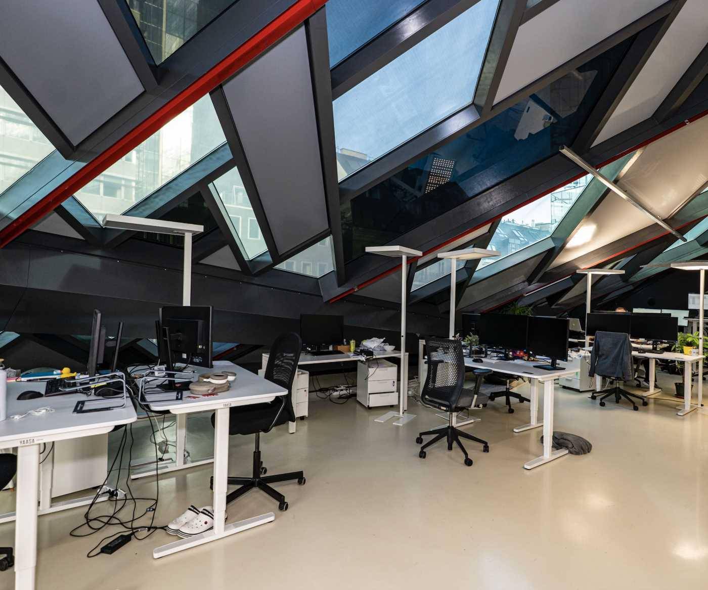 Moderner Büroraum mit einzigartiger Deckenkonstruktion, großen Fenstern und ergonomischen Arbeitsplätzen.