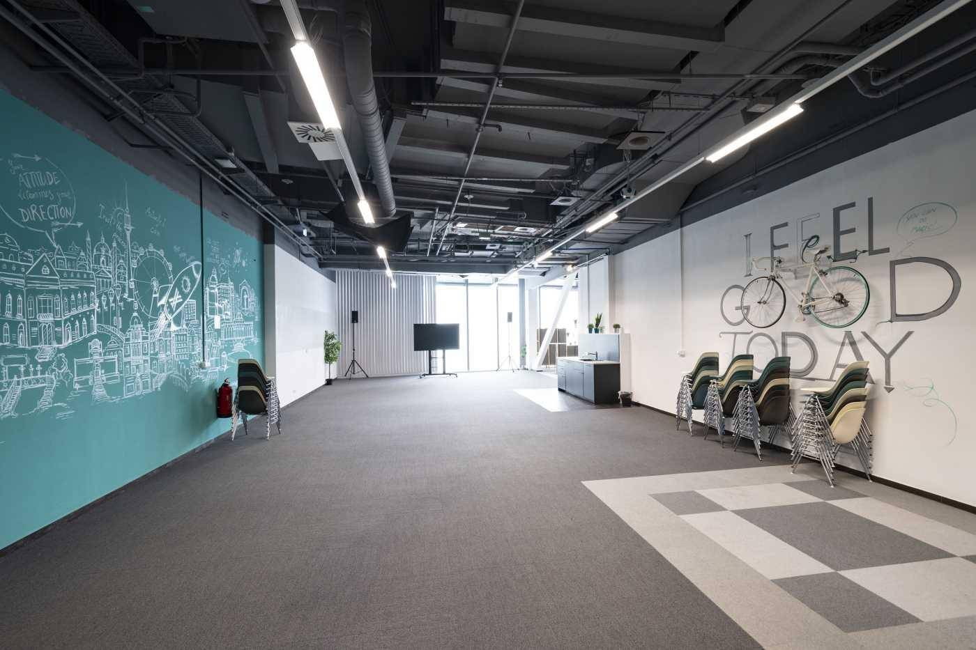 Großer, flexibler Raum mit Teppichboden, kreativen Wandmalereien und sichtbaren Deckeninstallationen.