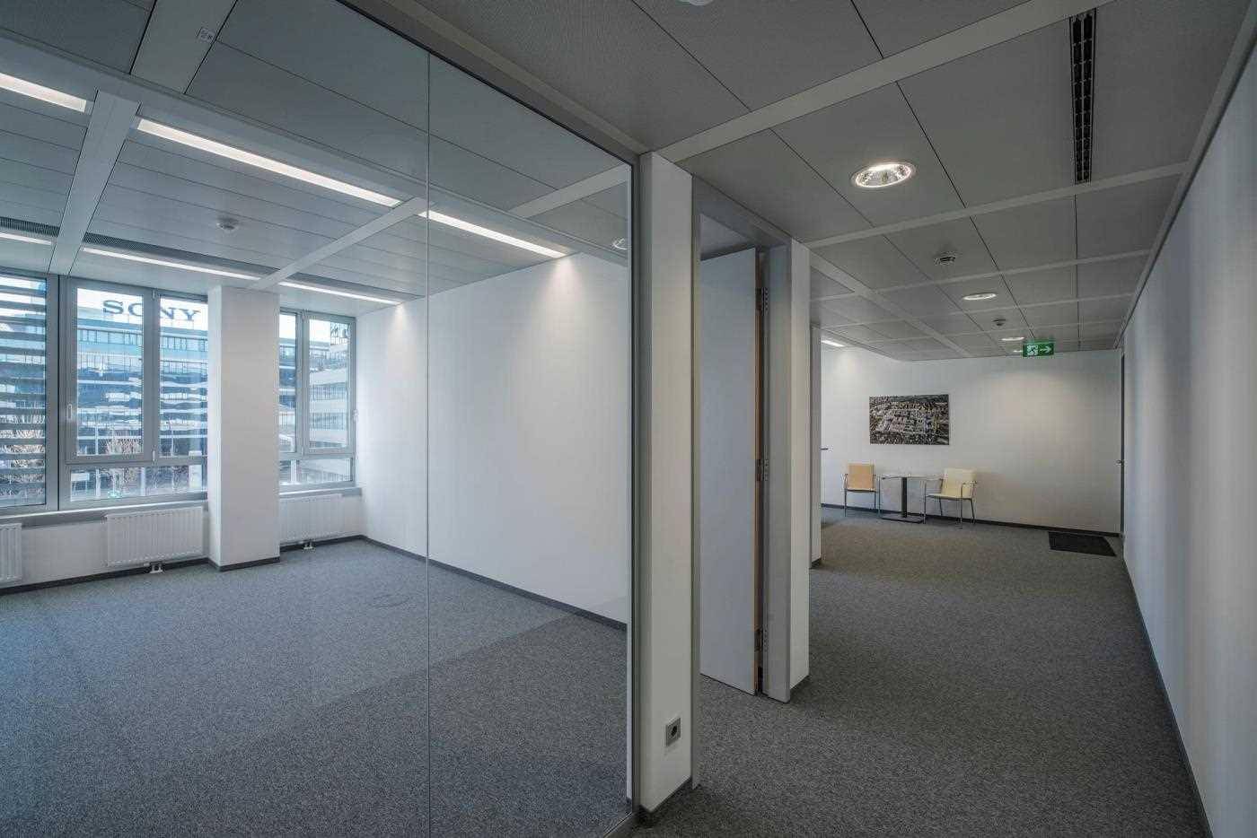 Leeres Büro mit Teppichboden, großen Fenstern und einem weiten Blick auf die umliegende Stadtlandschaft.