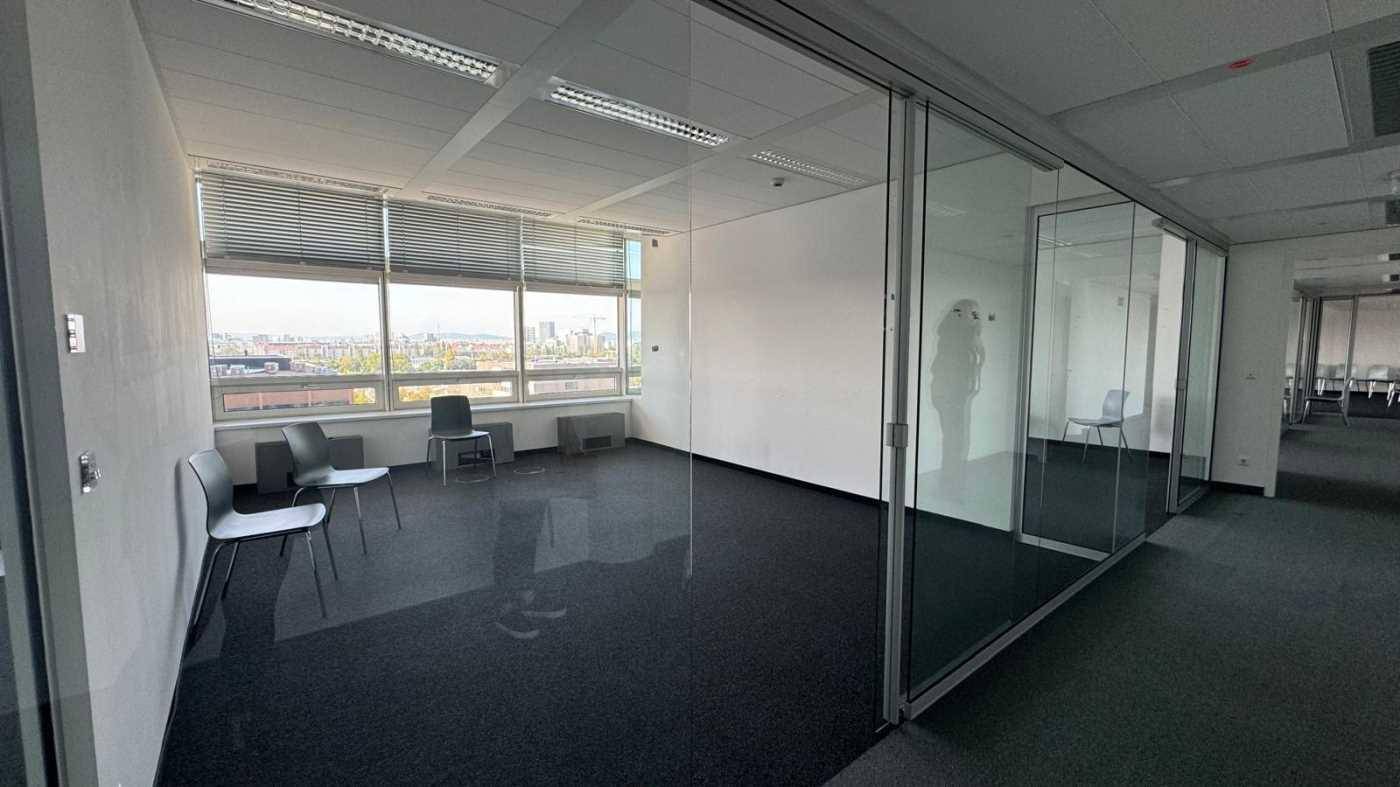 Heller Büroraum mit Teppichboden, Glaswänden und weitem Blick über die Stadt.