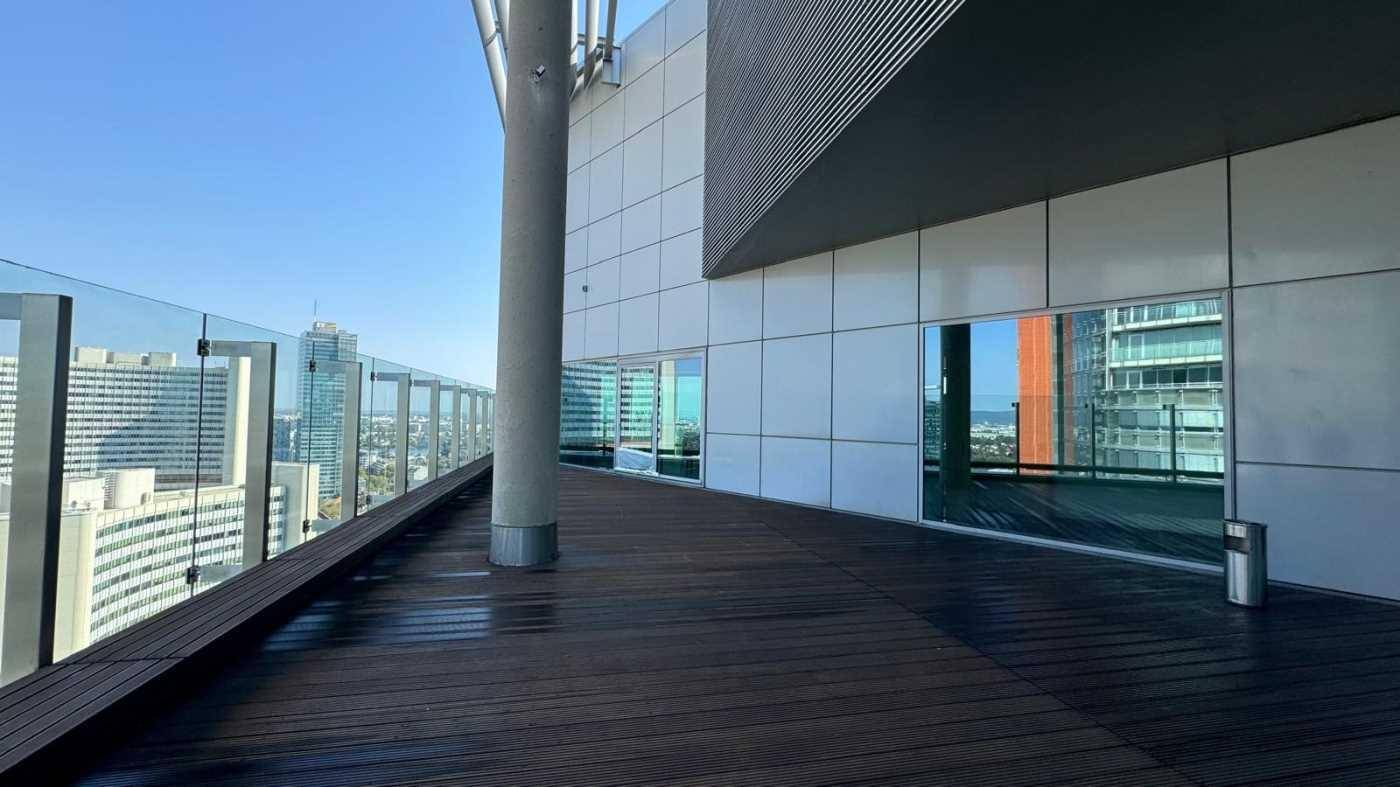 Eine weitläufige Dachterrasse mit Holzboden und Glasgeländer bietet einen beeindruckenden Blick über die Stadt.