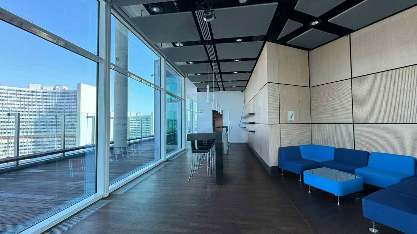Gemütlicher Loungebereich mit blauen Sofas, großen Fenstern und Zugang zu einer Terrasse mit Stadtblick.