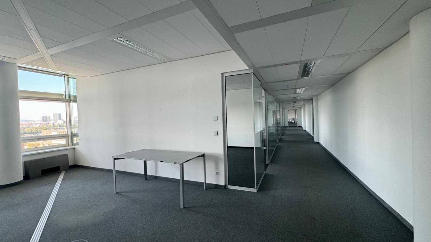 Leeres Büro mit Teppichboden, einem Tisch und Glaswänden, die separate Arbeitsbereiche abgrenzen.