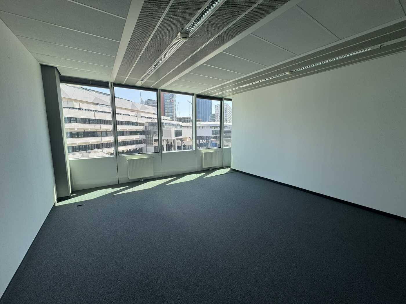 Geräumiger Bürobereich mit Teppichboden und großen Fenstern, die einen Blick auf die Stadt bieten.