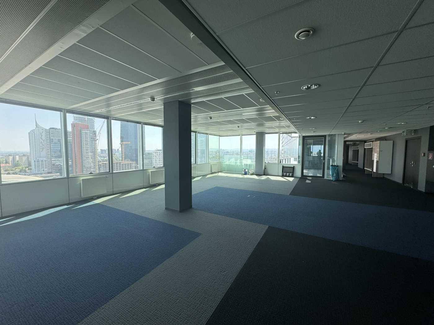 Großer offener Bürobereich mit gemustertem Teppichboden und weitem Blick auf die städtische Skyline.