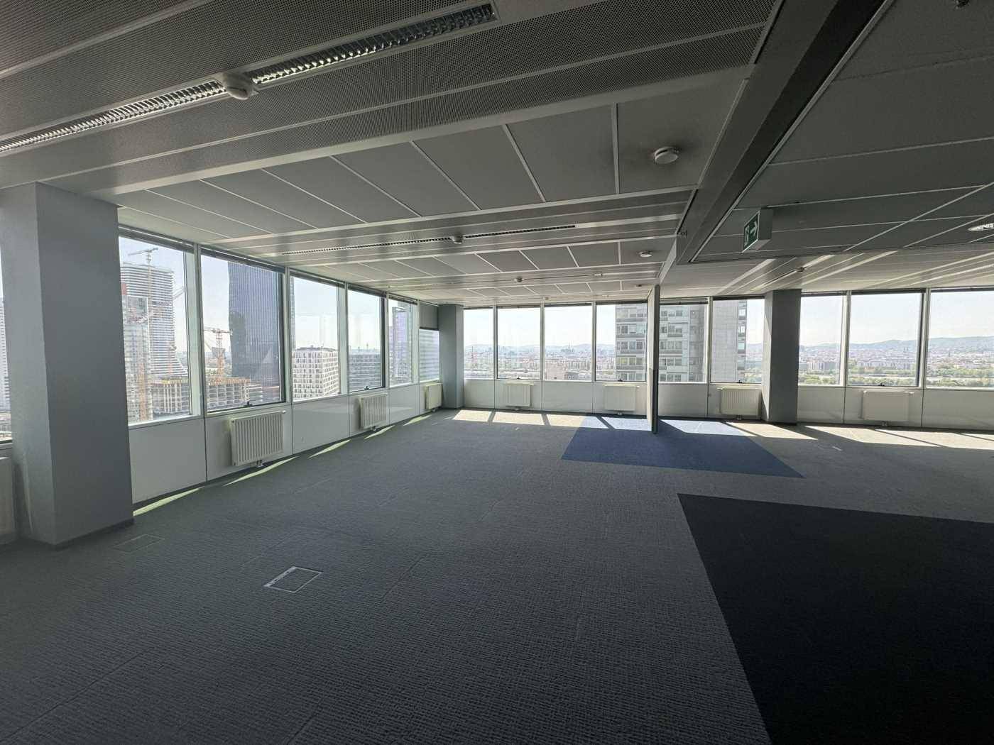 Großer offener Bürobereich mit grauem Teppichboden und weitem Blick auf die Stadt und Baustellen.