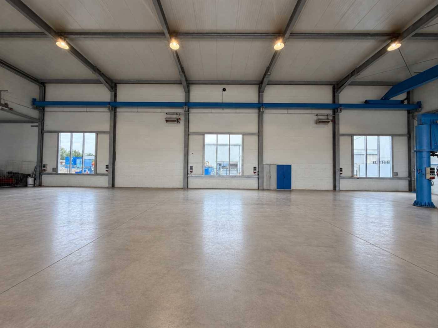 Innenansicht der Lagerhalle mit einer langen Fensterfront und einer blauen Tür, die für Helligkeit sorgt.