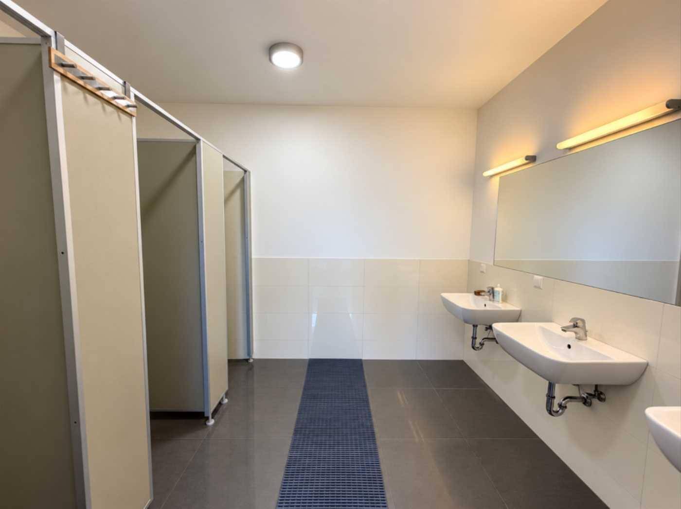 Geräumiger Waschraum mit mehreren Waschbecken, großen Spiegeln und Toilettenkabinen, sauber und funktional.