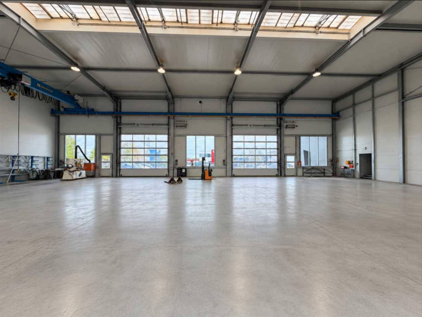 Helle Lagerhalle mit mehreren großen Rolltoren und Fenstern, die viel Tageslicht hereinlassen und Zugang bieten.