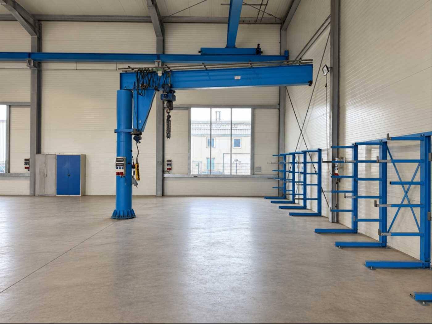 Innenansicht der Lagerhalle mit einem blauen Säulenschwenkkran und praktischen Kragarmregalen für Lagerzwecke.