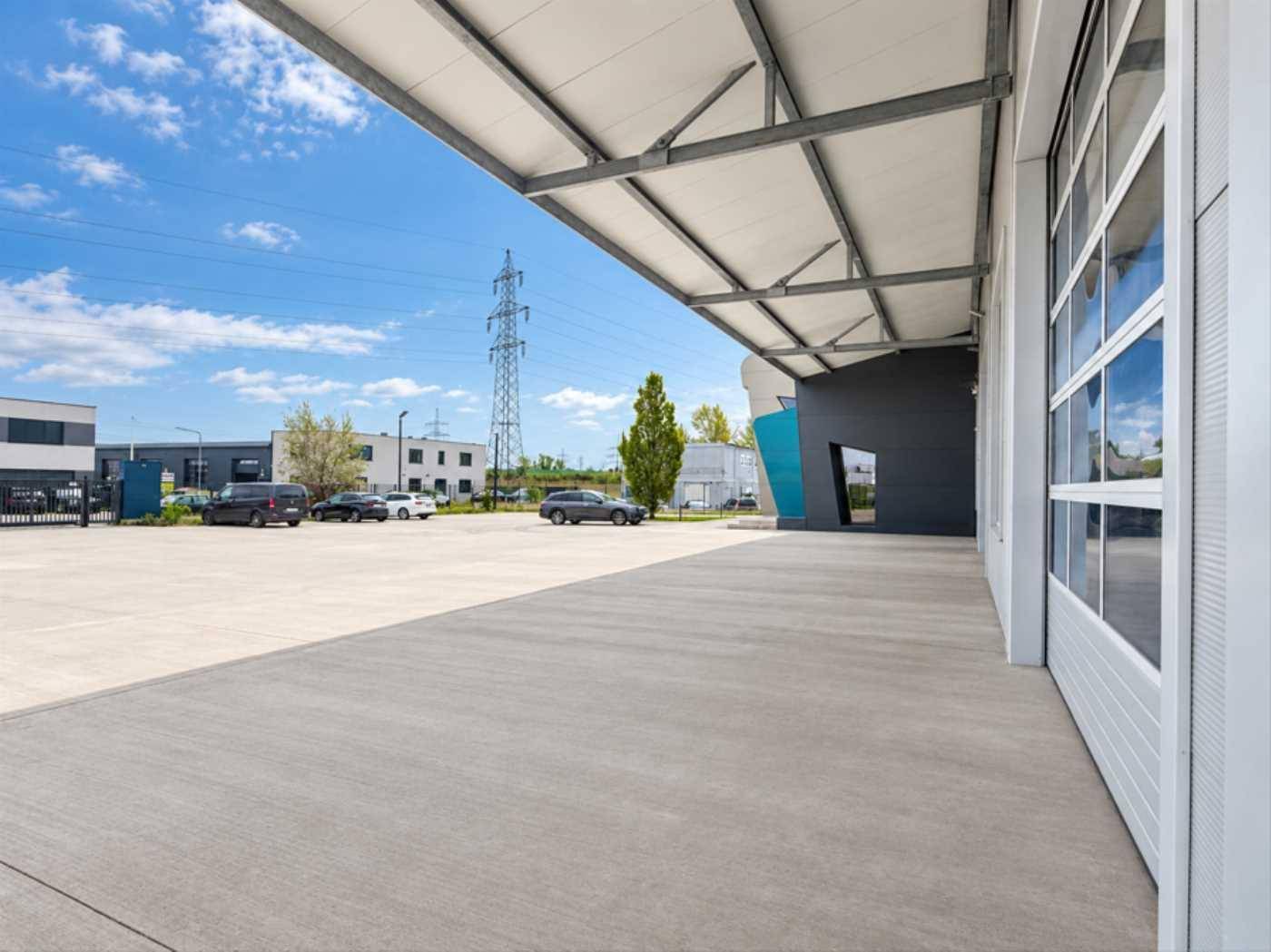 Weitläufiger Außenbereich des Industriegebäudes mit großem Betonvorplatz und Parkmöglichkeiten unter blauem Himmel.