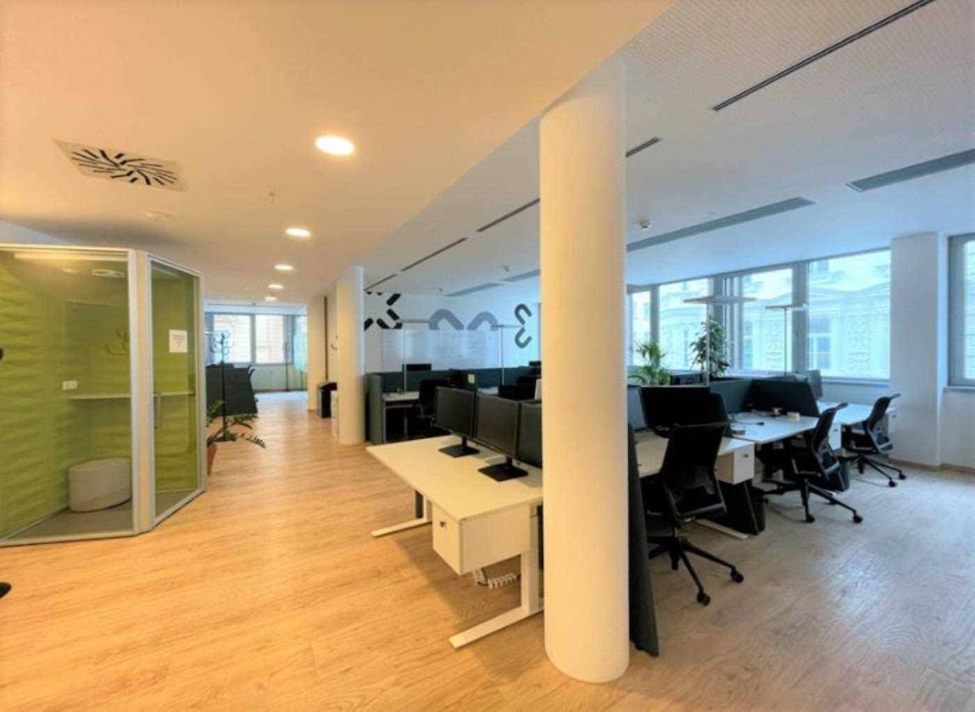 Weitläufiges Großraumbüro mit modernen Arbeitsplätzen, Säulen und schallgedämmten Telefonkabinen.