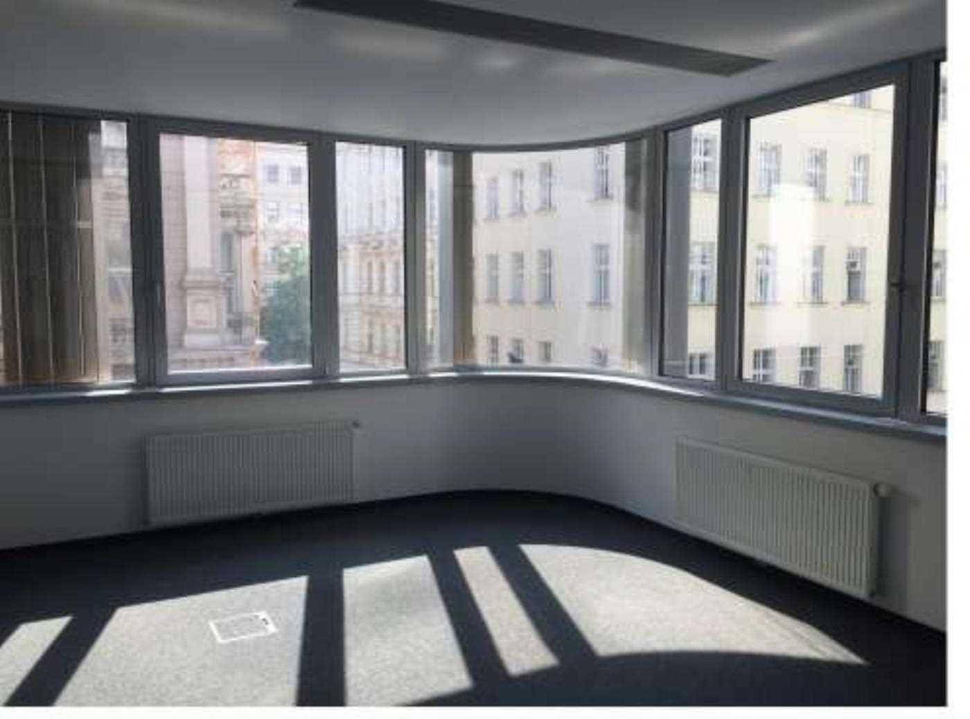 Heller Büroeckbereich mit geschwungenen Fenstern, Heizkörpern und Teppichboden, durchflutet von Sonnenlicht.